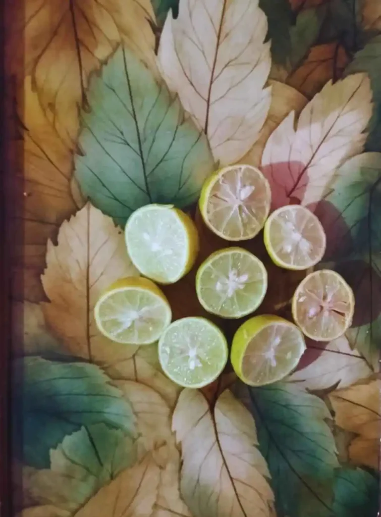 Eight halved lemons and limes arranged in a circle on a bed of colorful green and beige leaves, showing fresh citrus flesh and juice