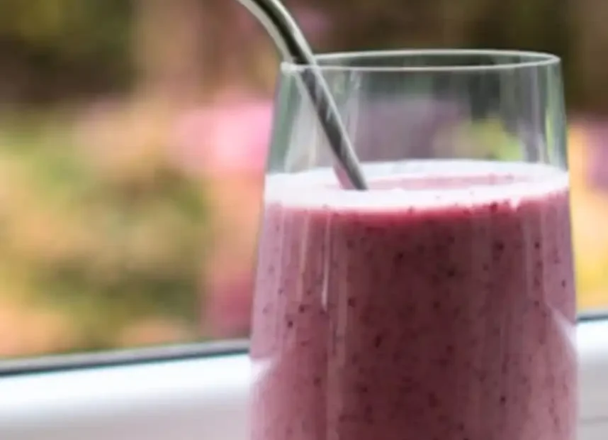 A tall glass of fresh pink strawberry smoothie with a metal straw, served with whole strawberries on a windowsill to illustrate the health benefits of strawberry smoothies.