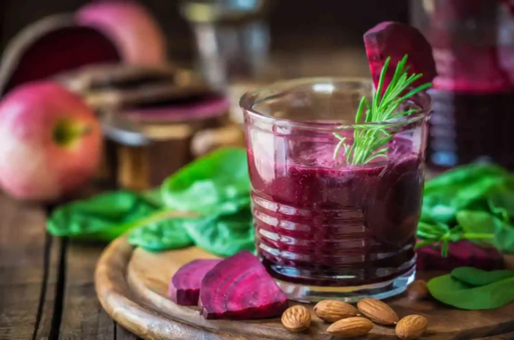 A glass of vibrant beetroot almond coconut milk smoothie garnished with rosemary, served on a wooden board with sliced beets, fresh spinach, and almonds.