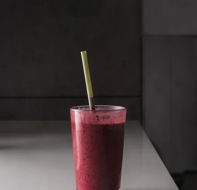 Beetroot and mixed berry smoothie in a glass with a straw, healthy antioxidant-rich drink on a white table.
